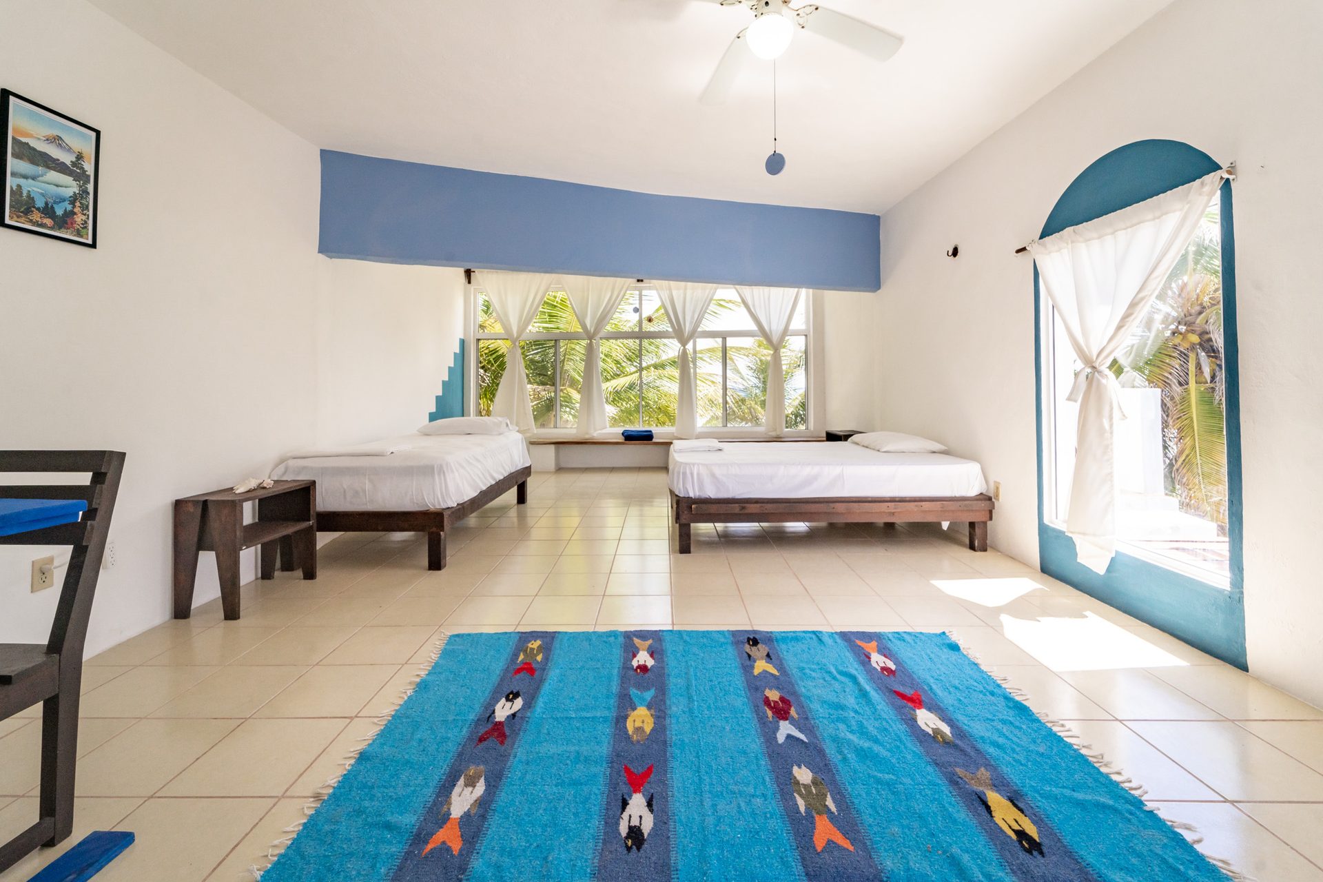 Room Water — two beds, blue fish rug, large windows with palms and sea